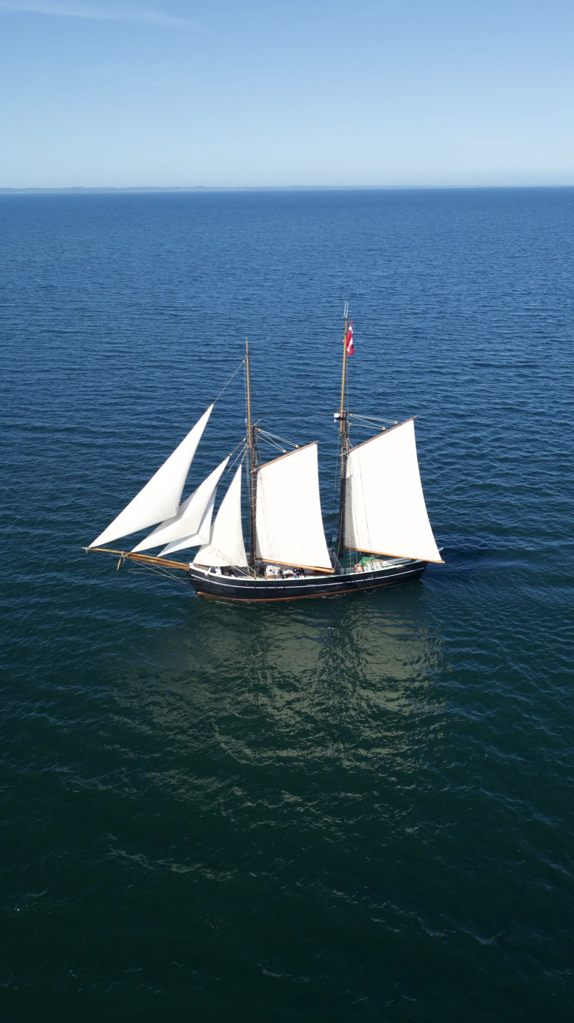 Aron under full sail on deep blue water, photographed from a drone