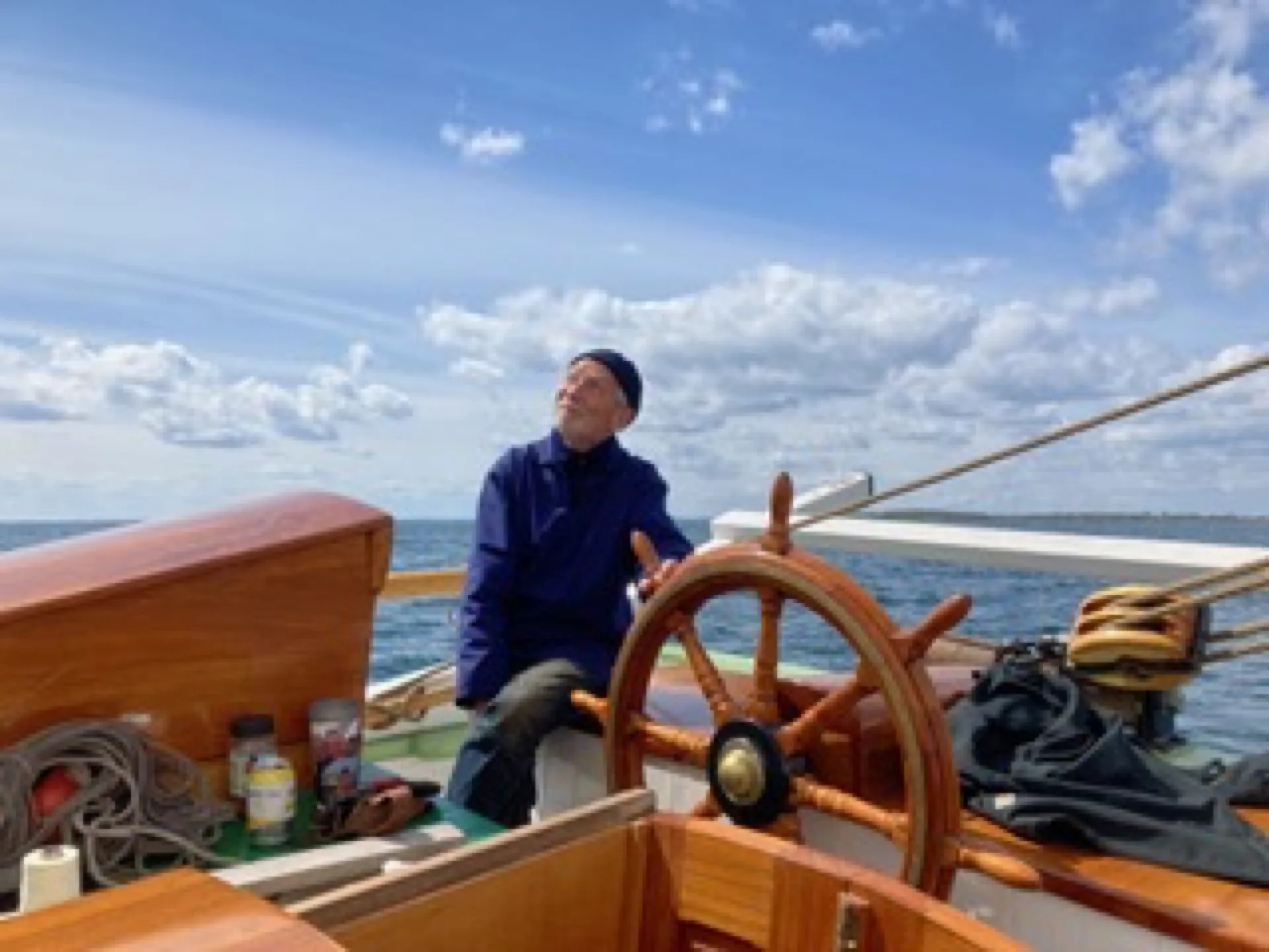 A guest steers Aron at the wooden wheel, looking up at the sails