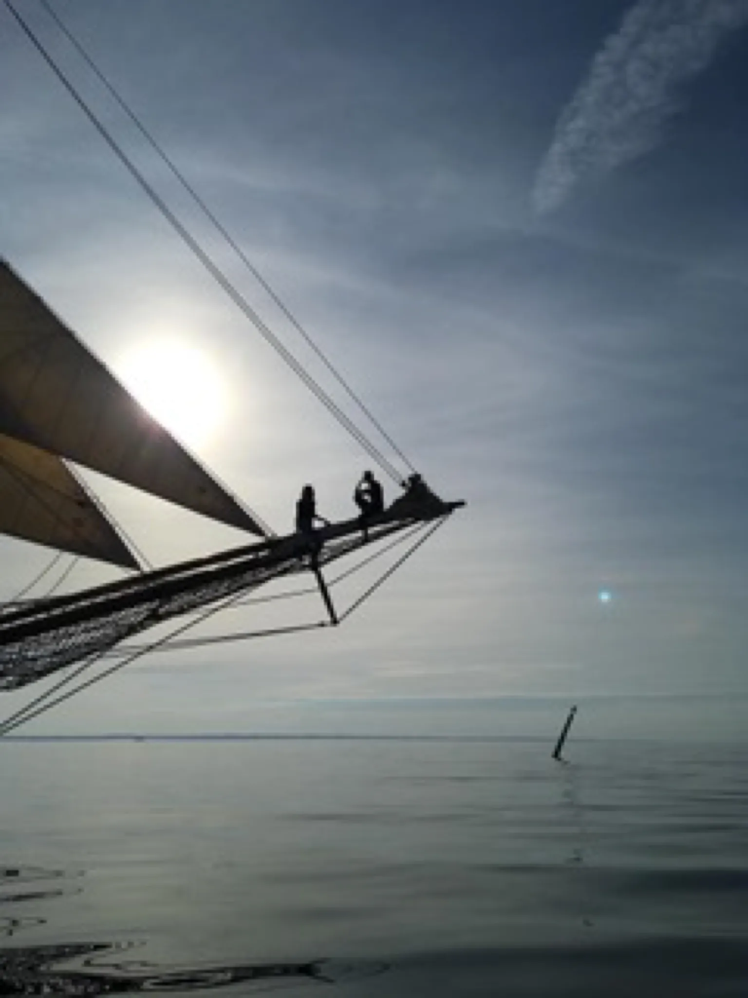 Two people silhouetted on Aron's bowsprit against the sun